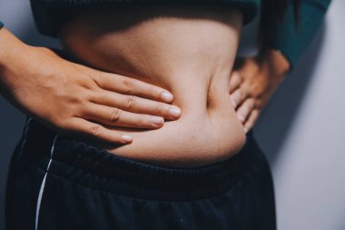 Asyalı kadın sol eliyle karnını çimdikliyor.