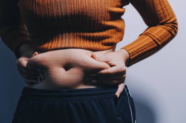 Asyalı kadın sol eliyle karnını çimdikliyor.