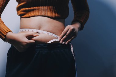 Asyalı kadın sol eliyle karnını çimdikliyor.