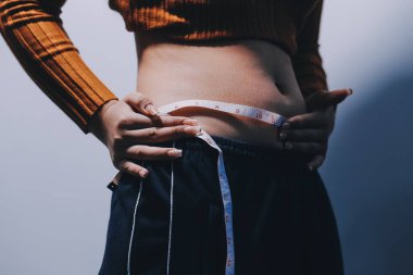 Asyalı kadın sol eliyle karnını çimdikliyor.