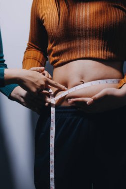 Asyalı kadın sol eliyle karnını çimdikliyor.