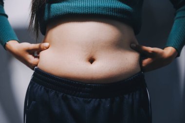 Asyalı kadın sol eliyle karnını çimdikliyor.