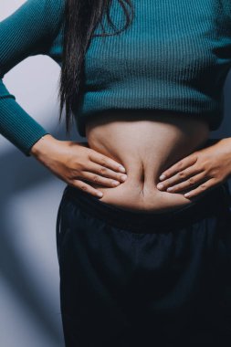 Asyalı kadın sol eliyle karnını çimdikliyor.