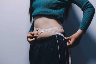 Asyalı kadın sol eliyle karnını çimdikliyor.