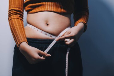 Asyalı kadın sol eliyle karnını çimdikliyor.