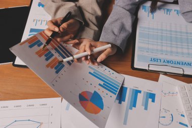 Group of confident business people point to graphs and charts to analyze market data, balance sheet, account, net profit to plan new sales strategies to increase production capacity.