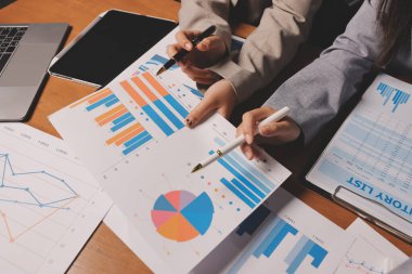 Group of confident business people point to graphs and charts to analyze market data, balance sheet, account, net profit to plan new sales strategies to increase production capacity.