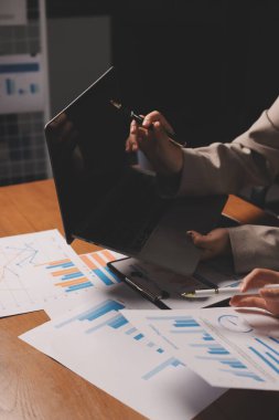 Group of confident business people point to graphs and charts to analyze market data, balance sheet, account, net profit to plan new sales strategies to increase production capacity.