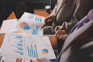 Group of confident business people point to graphs and charts to analyze market data, balance sheet, account, net profit to plan new sales strategies to increase production capacity.