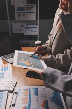 Group of confident business people point to graphs and charts to analyze market data, balance sheet, account, net profit to plan new sales strategies to increase production capacity.