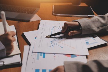 Group of confident business people point to graphs and charts to analyze market data, balance sheet, account, net profit to plan new sales strategies to increase production capacity.