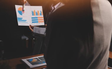 Group of confident business people point to graphs and charts to analyze market data, balance sheet, account, net profit to plan new sales strategies to increase production capacity.