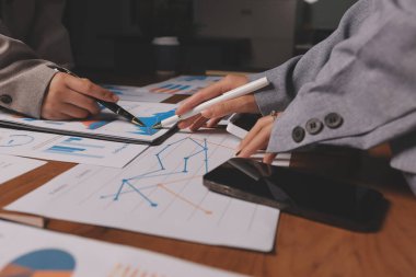 Group of confident business people point to graphs and charts to analyze market data, balance sheet, account, net profit to plan new sales strategies to increase production capacity.