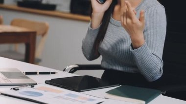 Ofisteki kadın akıllı telefonuyla bilgisayarla çalışıyor. Masasında çalışan genç bir iş kadını..