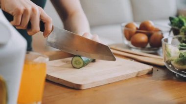 Ahşap kesim tahtasında salatayla salatalık kesen kadın.