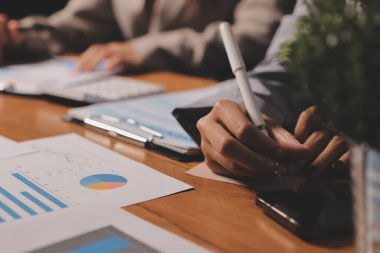 Group of confident business people point to graphs and charts to analyze market data, balance sheet, account, net profit to plan new sales strategies to increase production capacity.