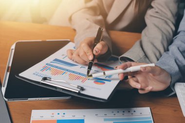 Group of confident business people point to graphs and charts to analyze market data, balance sheet, account, net profit to plan new sales strategies to increase production capacity.