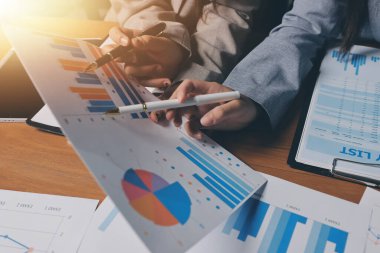 Group of confident business people point to graphs and charts to analyze market data, balance sheet, account, net profit to plan new sales strategies to increase production capacity.