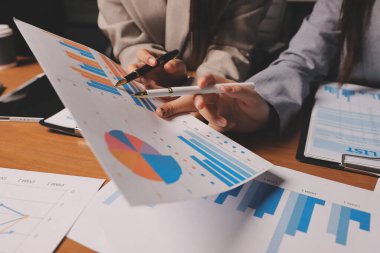 Group of confident business people point to graphs and charts to analyze market data, balance sheet, account, net profit to plan new sales strategies to increase production capacity.