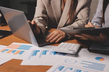 Group of confident business people point to graphs and charts to analyze market data, balance sheet, account, net profit to plan new sales strategies to increase production capacity.