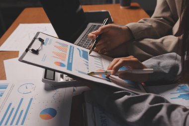 Group of confident business people point to graphs and charts to analyze market data, balance sheet, account, net profit to plan new sales strategies to increase production capacity.