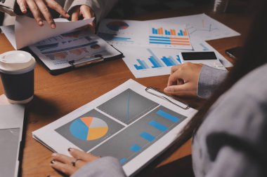 Group of confident business people point to graphs and charts to analyze market data, balance sheet, account, net profit to plan new sales strategies to increase production capacity.