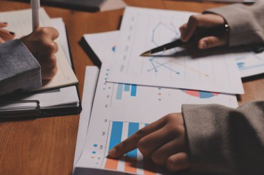 Group of confident business people point to graphs and charts to analyze market data, balance sheet, account, net profit to plan new sales strategies to increase production capacity.