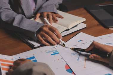 Group of confident business people point to graphs and charts to analyze market data, balance sheet, account, net profit to plan new sales strategies to increase production capacity.