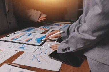 Group of confident business people point to graphs and charts to analyze market data, balance sheet, account, net profit to plan new sales strategies to increase production capacity.