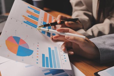 Group of confident business people point to graphs and charts to analyze market data, balance sheet, account, net profit to plan new sales strategies to increase production capacity.