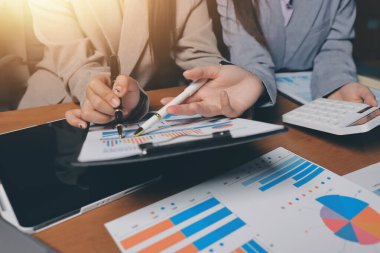 Group of confident business people point to graphs and charts to analyze market data, balance sheet, account, net profit to plan new sales strategies to increase production capacity.