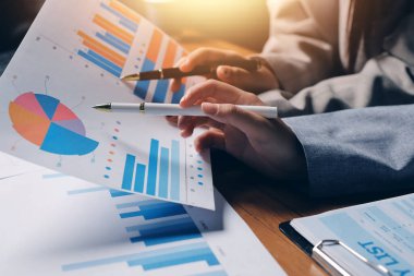 Group of confident business people point to graphs and charts to analyze market data, balance sheet, account, net profit to plan new sales strategies to increase production capacity.