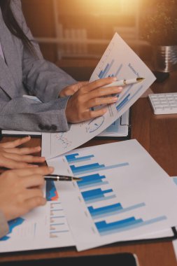 Group of confident business people point to graphs and charts to analyze market data, balance sheet, account, net profit to plan new sales strategies to increase production capacity.