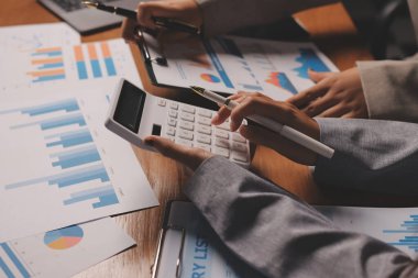 Group of confident business people point to graphs and charts to analyze market data, balance sheet, account, net profit to plan new sales strategies to increase production capacity.