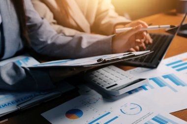 Group of confident business people point to graphs and charts to analyze market data, balance sheet, account, net profit to plan new sales strategies to increase production capacity.