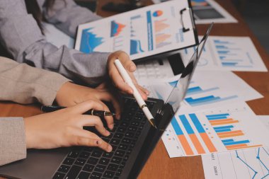 Group of confident business people point to graphs and charts to analyze market data, balance sheet, account, net profit to plan new sales strategies to increase production capacity.