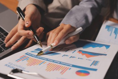 Group of confident business people point to graphs and charts to analyze market data, balance sheet, account, net profit to plan new sales strategies to increase production capacity.