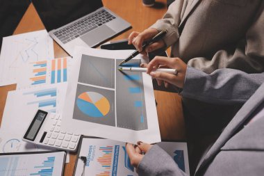 Group of confident business people point to graphs and charts to analyze market data, balance sheet, account, net profit to plan new sales strategies to increase production capacity.