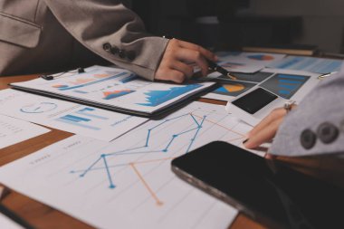 Group of confident business people point to graphs and charts to analyze market data, balance sheet, account, net profit to plan new sales strategies to increase production capacity.