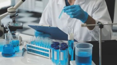 Koruyucu eldivenlerdeki bilim adamları laboratuarda sıvı test tüpleri tutuyorlar.