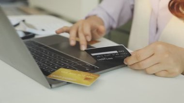 Genç bir kadın kredi kartı tutuyor ve online alışveriş için dizüstü bilgisayar kullanıyor.
