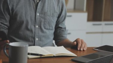Adam akıllı telefon tutuyor ve evde çalışırken defter kullanıyor.
