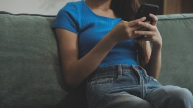 Evdeki koltukta cep telefonu kullanan bir kadın. Oturma odasında cep telefonu olan genç bir kadın, yaşam tarzı..