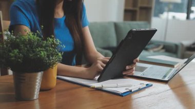 Ofisteki not defterine tablet bilgisayar kullanan ve yazan genç bir kadın.