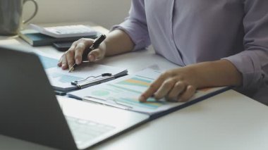 Bilgisayarda çalışan genç bir kadın ve ofiste çalışan belgeler, yakın plan.