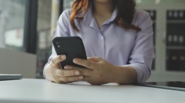 Ofiste masada otururken cep telefonu kullanan genç bir kadın. Modern ofiste otururken akıllı telefon kullanan genç bir kadının görüntüsünü kapat..