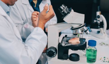 Laboratuvardaki Asyalı bilim adamları mikroskop ve laboratuvar ekipmanları kullanarak gıda araştırmaları yapıyor, gıda bilimi ve biyoteknoloji alanında yenilikler sergiliyorlar.