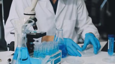 Koruyucu kıyafetli ve maskeli bilim adamı deney tüpü ve sıvı tutuyor.