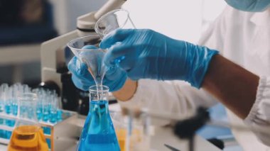 Mavi üniformalı bilim adamı laboratuarda sıvıyla deney yapıyor..
