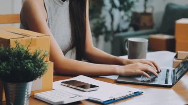 Genç Asyalı kadın paketleri dizüstü bilgisayar ve internetten müşterileri teslim etmek için kontrol ediyor. Ev servisi kavramı.